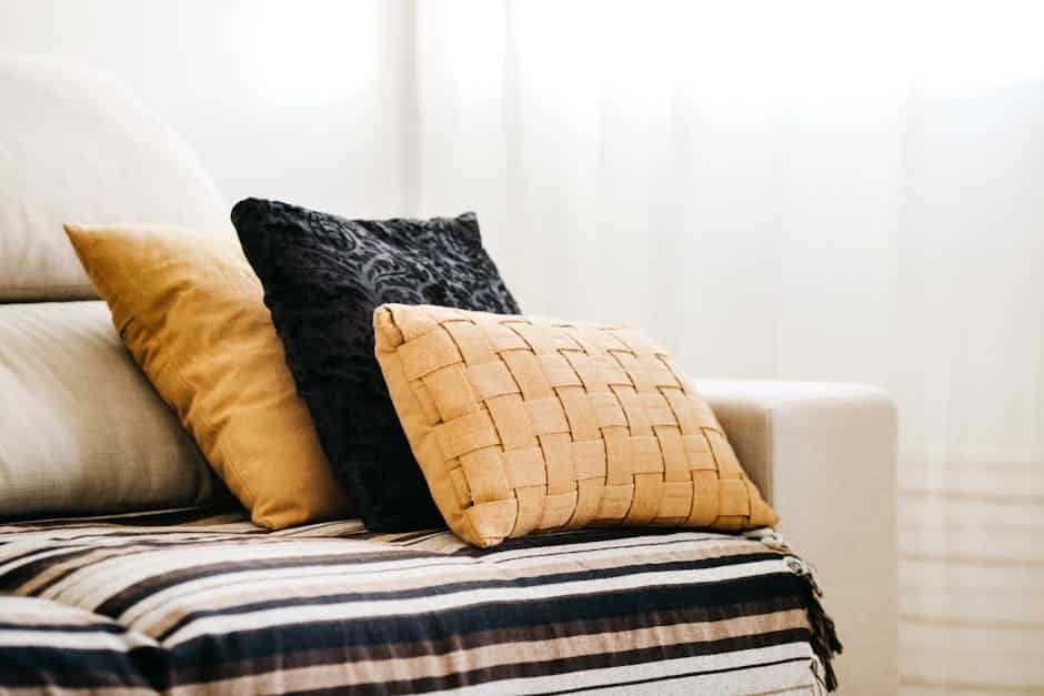 Coussins ocre et plaid rayé sur un canapé clair, tendance déco aux couleurs chaudes